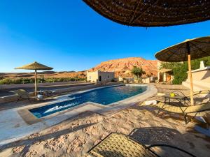 a swimming pool with chairs and umbrellas in the desert at Dar Bikouch in Aït Benhaddou