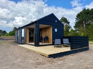 a black tiny house with two chairs on a wooden deck at Feriebyens Spahuse in Rødvig