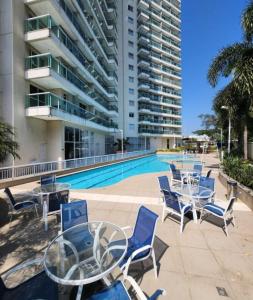 a swimming pool with chairs and tables and a building at Flat & Suite Premium - Rio Centro - Barra - Farmasi Arena in Rio de Janeiro
