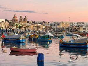 a group of boats in the water with a city in the background at Seaview Marsaxlokk Apartment Eye of Osiris in Marsaxlokk