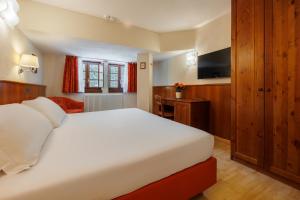 a bedroom with a large white bed and a television at iH Hotels Courmayeur Mont Blanc in Courmayeur