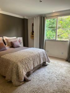 a bedroom with a bed and a window with a guitar at Apartamento Charmoso e Tranquilo para sua Estadia in Vargem Alta