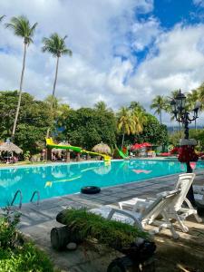 a swimming pool with two white chairs and palm trees at Hotel Pasabien in Huité