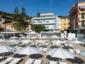 a group of white chairs and umbrellas on a beach at Acciuga Hotel in Laigueglia