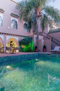 a swimming pool in front of a house with a palm tree at Kasbah La Moun - The Art Of Hospitality in Marrakesh