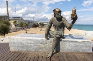 a statue of a man sitting on a wall next to the beach at Badalona Old Town Dalt de la Vila in Badalona