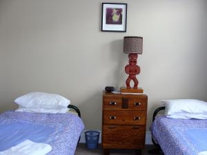 a bedroom with two beds and a lamp on a dresser at Oamaru Pink Cottage in Oamaru