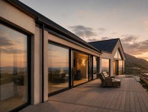 a house with a deck with a view of the mountains at Luxury Glass Villa with Hot Tub & Sea Views - Connemara in Roundstone