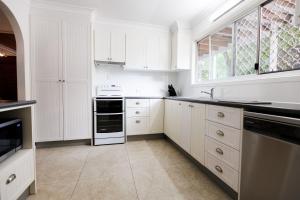 a white kitchen with white cabinets and a window at Family & Friends Cottage in Mount Tamborine