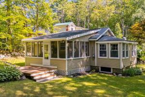 a yellow tiny house with a porch in a yard at Sebago Shores Cottage in North Sebago
