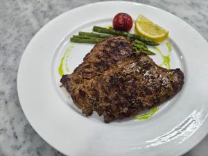 a white plate with a piece of meat and asparagus at Serenata Korcare Resort in Tirana