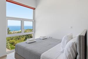 a white bedroom with a bed and a large window at Celestial Luxury Residences in Asgourou