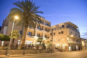 a large white building with palm trees in front of it at Hotel Corallo New in Muravera