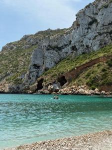 two people swimming in the water next to a mountain at Apartamento vacacional Jávea in Jávea