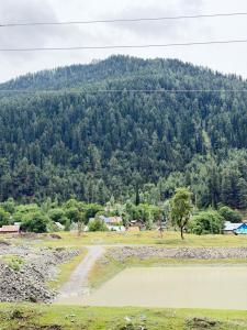 a field with a body of water in front of a mountain at Himalayan Stay in Sonāmarg