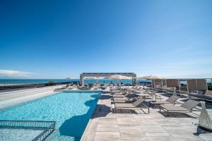 a swimming pool with chairs and umbrellas next to the ocean at Residence Diana Seafront in Bibione