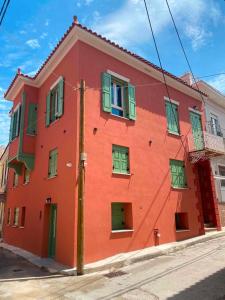 a red building with green windows on a street at Makaros Nissos City in Mytilene