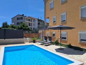 a swimming pool with an umbrella and two chairs and a building at Apartment Vukadin in Pula
