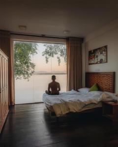 a man sitting on a bed in a bedroom with a large window at Peacock Wild YALA in Tissamaharama