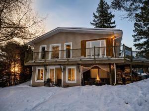 a large house in the snow with a deck at Chalet Cozy Spa sur Lac in Saint-André-Avellin