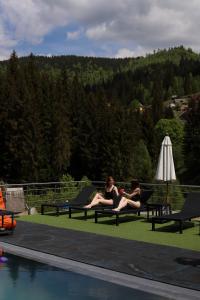 two women sitting on benches next to a swimming pool at Silveroks Hotel in Bukovel