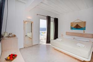 a white bedroom with a bed and a balcony at Aegean View Suites Mykonos in Agios Stefanos