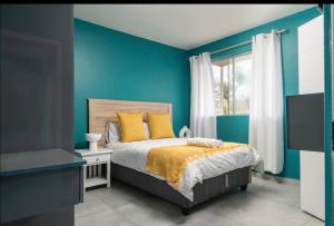 a bedroom with blue walls and a bed with yellow pillows at 94 Camarque Umdloti in Umdloti