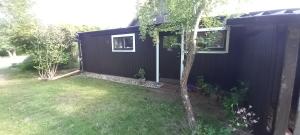 a black house with a yard with a tree at Stuga PETEL in Färjestaden