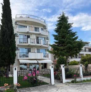 a white building with a fence and a tree at HOTEL BRIZ - Free Parking in Burgas
