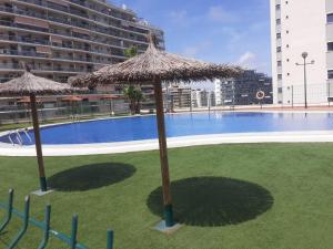 two straw umbrellas in the grass near a swimming pool at Relaxe La cala in Villajoyosa