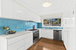 a kitchen with white cabinets and blue walls at Mariners in the Village in Shellharbour