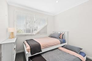 a white bedroom with two beds and a window at Mariners in the Village in Shellharbour