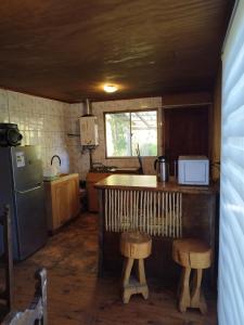 a kitchen with a counter and a refrigerator and stools at Puñañas descanso y experiencias in Vilcún