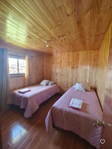 a bedroom with two beds in a wooden room at Cabaña Queule Costero in Queule