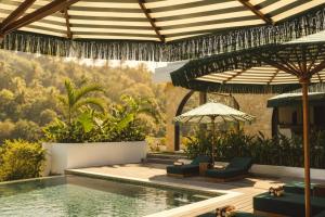 an outdoor pool with chairs and an umbrella at Kanalla Boutique Hotel - Adults Only in Kuta Lombok