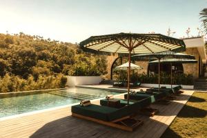 a row of lounge chairs with umbrellas next to a swimming pool at Kanalla Boutique Hotel - Adults Only in Kuta Lombok