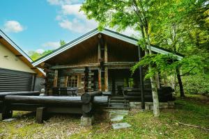 a log cabin with a porch in the woods at Log Hotel The Maple Lodge in Iwamizawa