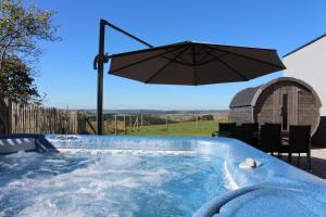 a jacuzzi tub with an umbrella in a yard at Eifel-Dream Schneifelhaus in Kobscheid
