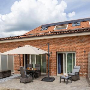 a patio with an umbrella and chairs and a table at Gulfhof bei Kletzsch Apartments & Ferienwohnungen in Großefehn Ostfriesland in Großefehn 