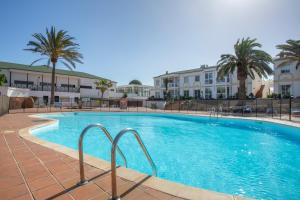 a large swimming pool with palm trees and buildings at Piccola Oasi Corralejo in Corralejo