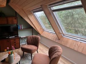 a living room with two chairs and a tv and two windows at Gastenverblijf Boven De S l a g e r i j in Schijndel