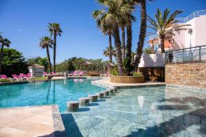 a swimming pool with palm trees and pink chairs at Grand Hôtel Les Flamants Roses Thalasso & Spa in Canet-en-Roussillon