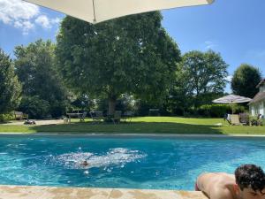 a man laying in a swimming pool under an umbrella at La Corti in Tillières-sur-Avre
