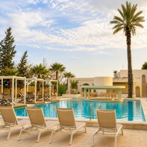 a resort pool with chairs and a palm tree at Hôtel Archipel in Monastir