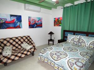 a bedroom with a bed and a couch and paintings at Artist Room Curaçao in Willemstad