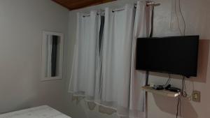 a bedroom with a television and a white curtain at Suítes Dona Ilda in Pirenópolis