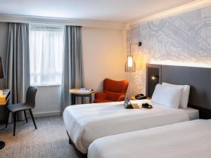 a hotel room with two beds and a chair at Mercure Birmingham West Hotel in West Bromwich +103 photos