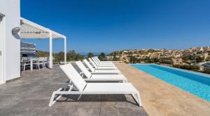 a row of white lounge chairs next to a swimming pool at Villa Ghea - Indoor Jacuzzi Pool, Sauna and Games Room in Mellieħa