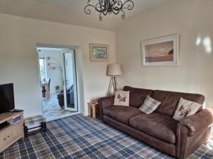 a living room with a brown couch and a tv at Beautiful 2-Bed semi rural cottage enclosed garden in Drummore