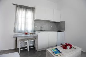 a kitchen with white cabinets and a sink and a table at Flora & Agelos Studios - Paros in Chrissi Akti